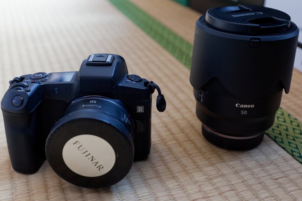 フードを付けたレンズを立てて置き、ボディの横に並べて大きさを比べた写真