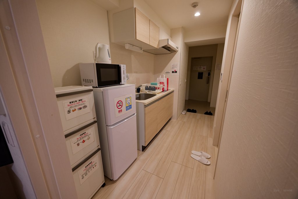 冷蔵庫、電子レンジ、電気ケトル、流し台が並ぶ宿の部屋のキッチン