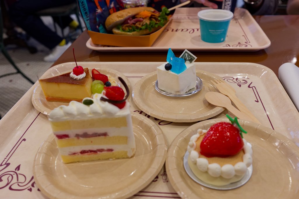 トレーに並んだ4個のケーキ。ショートケーキ、フルーツを添えたプリンケーキ、いちごのタルト、青いゼリーをのせた白いケーキ